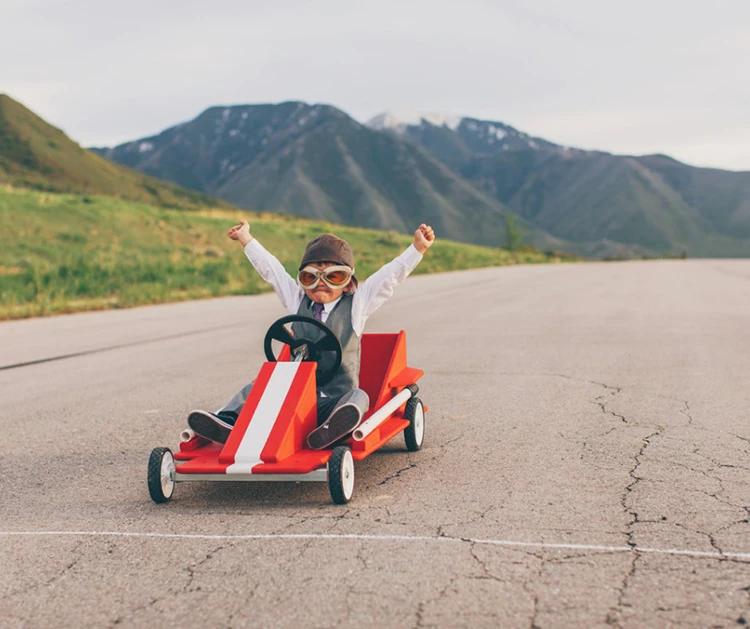 Child driving a toy go-kart, arms raised in excitement