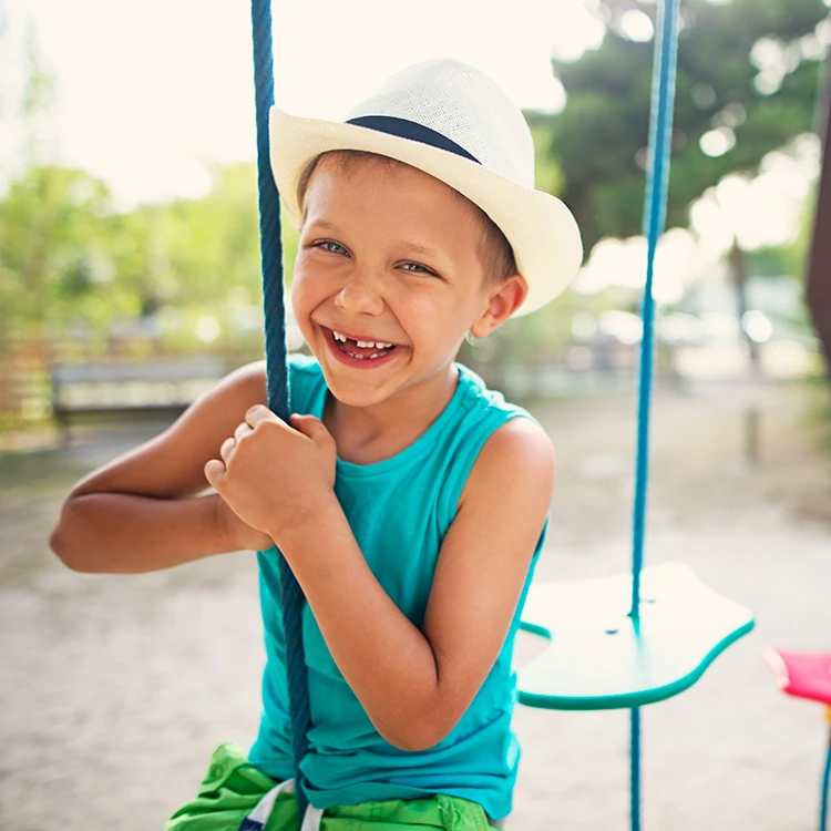 Young boy in a sun hat smiling on a playground swing